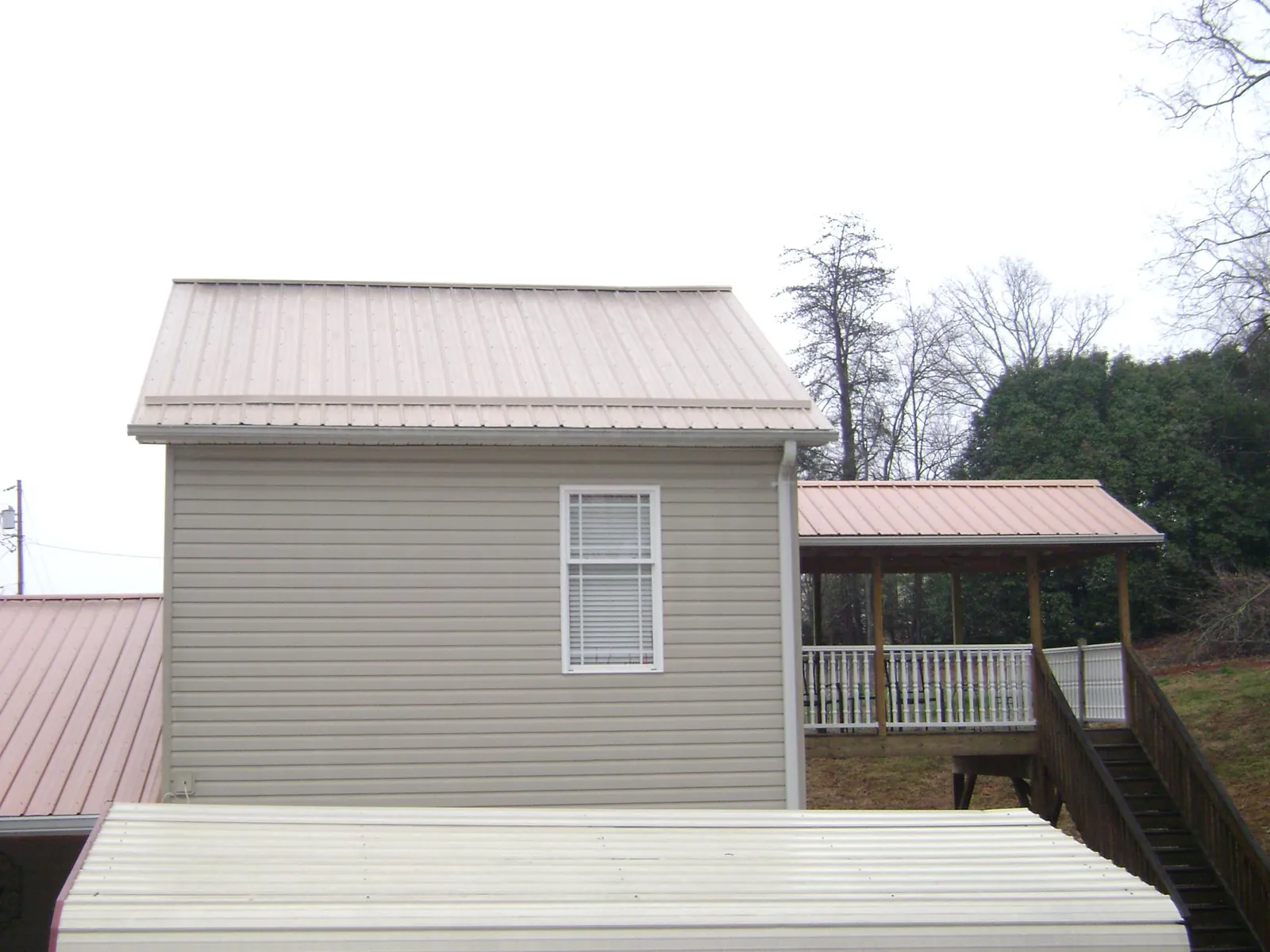 Tan metal roofs on a two story addition and attached porch, from a Roof Replacement job in Dana